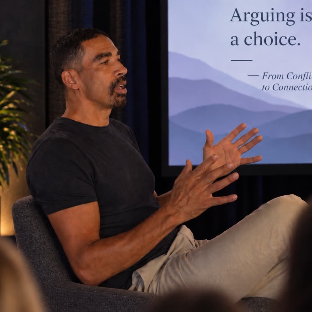 Micah Salaberrios speaking, seated beside a slide that reads “Arguing is a choice,” from From Conflict to Connection